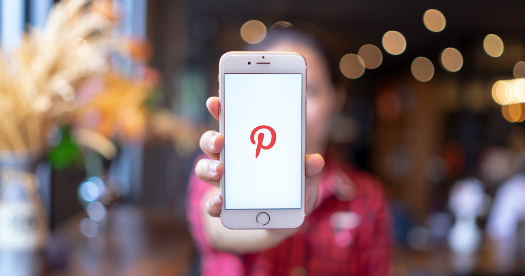 A person holding up a phone with the Pinterest logo on it, featuring a discount code for the PlanetHoster WordPress plugin.